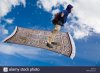 man-on-a-magic-carpet-flying-down-across-blue-sky-with-white-clouds-D497JE.jpg